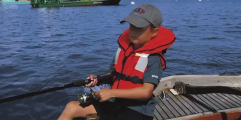 Un enfant pêche en mer, portant un gilet de sauvetage obligatoire. La question du gilet de sauvetage obligatoire jusqu'à quel âge est cruciale pour la sécurité nautique.