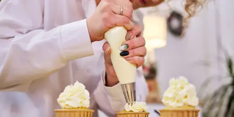 Une pâtissière décore des cupcakes avec une chantilly mascarpone aérienne.