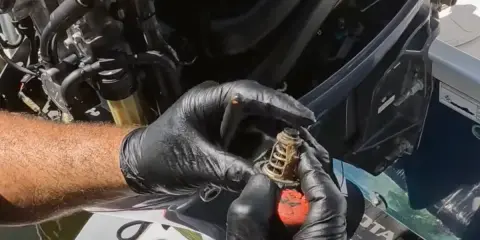 Mains gantées tenant un thermostat usagé, prêt pour le changement sur un moteur hors bord Yamaha.