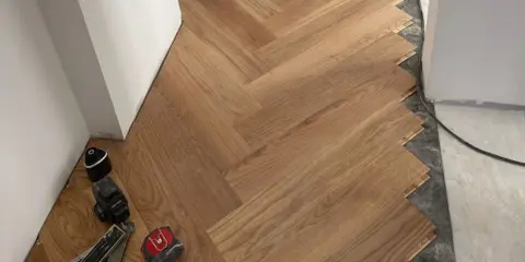 Instalación de suelo de madera en espiga. El rodapié igual que el suelo crea un acabado moderno y continuo. Herramientas de instalación a la vista.