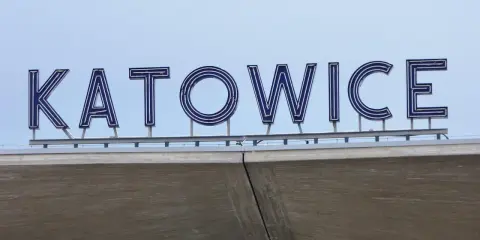 Napis "KATOWICE" z niebieskimi neonami na tle nieba, nad betonową konstrukcją.