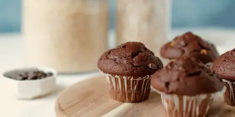 Wilgotne i puszyste muffinki czekoladowe, idealne na każdy dzień. Składniki do ich przygotowania w tle.