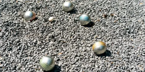 Boules de pétanque argentées, certaines rayées de couleurs vives, reposent sur un lit de gravier gris. Le jeu de pétanque est prêt à commencer.