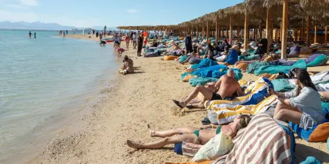 Słoneczna plaża w Egipcie w maju. Ludzie odpoczywają na leżakach pod palmowymi parasolami, ciesząc się piękną pogodą.