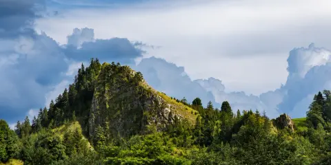 Górzysty krajobraz rezerwat przyrody Biała Woda. Skaliste zbocze porośnięte drzewami, na tle burzowych chmur.