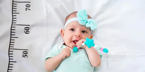 Un bebé sonriente con un chupete de estrella turquesa, con una cinta azul en la cabeza. A su lado, una regla marca el crecimiento, ¡un bebé perceptible!