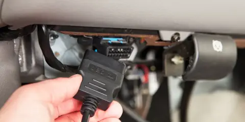 Ręka podłącza kabel OBD II do złącza diagnostycznego pojazdu, aby sprawdzić błędy DTC.
