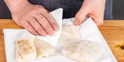 Hände tupfen Steinbeißer Fischfilets auf Küchenpapier trocken, bereit für die Zubereitung.