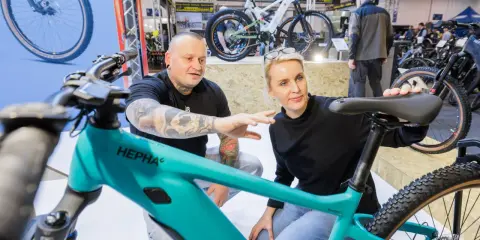 Ein Mann mit Tattoos und eine Frau begutachten auf der Fahrrad Messe ein türkisfarbenes E-Bike.