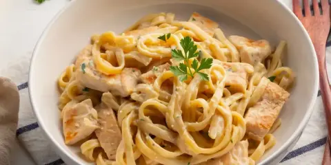 Pyszne makaron tagliatelle z kurczakiem w kremowym sosie, udekorowane natką pietruszki. Idealne danie na obiad.