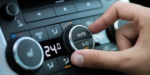 Dedo ajustando el dial del aire acondicionado del coche para comprobar el compresor. Se ve la pantalla digital con 24.0 grados.