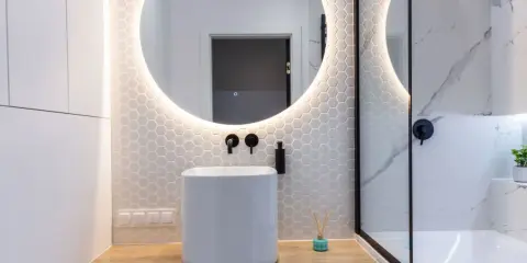 Baño moderno con lavabo blanco, espejo redondo con luz LED y azulejos hexagonales. ¿Cuánto cuesta reformar un baño así?