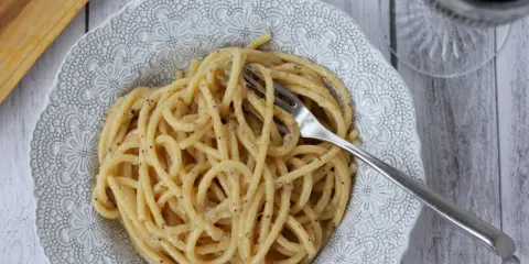 Porcja pysznego cacio e pepe z widelcem w talerzu, gotowa do zjedzenia.