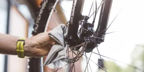Ręka z żółtym zegarkiem czyści tarczę hamulcową roweru, by uniknąć piszczących hamulców w rowerze.