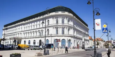 Elegancki, biały budynek w centrum Warszawy, być może najdroższy hotel w Warszawie. Słoneczny dzień, ruch uliczny.