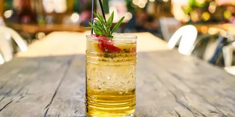 Orzeźwiający drink z wódką waniliową, lodem, owocami i gałązką rozmarynu na drewnianym stole.