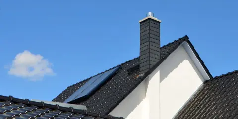 Nowoczesny komin na dachu z czarnej dachówki, z panelem słonecznym. Jaka średnica komina do pieca na drewno?