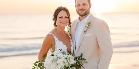 Groom in a tan suit, perfect for what to wear to beach wedding male, smiles with bride holding bouquet at sunset.