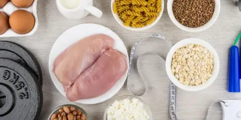 Składniki na dietę na masę mięśniową: kurczak, jajka, mleko, płatki owsiane, makaron, kasza gryczana, orzeszki ziemne, twaróg, hantle i skakanka.