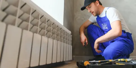 Técnico revisa la **presión de la caldera** junto a un radiador blanco. Herramientas a su lado.