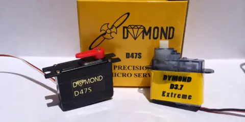Zwei Servos, ein schwarzer Dymond D47S und ein gelber Dymond D3.7 Extreme, stehen vor einer gelben Box mit der Aufschrift "Dymond D47S".