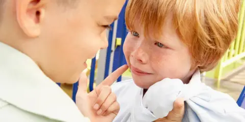 Ein Junge zeigt mit dem Finger auf das Gesicht eines anderen Jungen, der verängstigt wirkt. Ein Beispiel für Mobbing in der Schule.