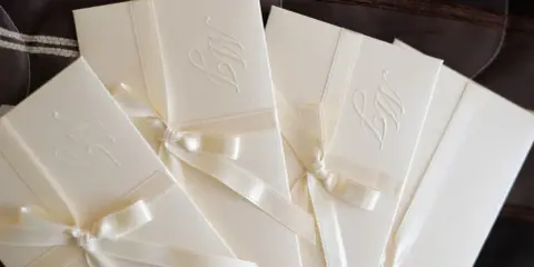 Eleganckie zaproszenia ślubne z monogramem, ozdobione satynową wstążką. Idealne, by dowiedzieć się, jak zrobić zaproszenie w Wordzie.