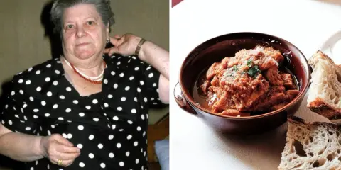 Una donna con un vestito a pois guarda verso la telecamera, accanto a una ciotola di trippa alla romana con pane.