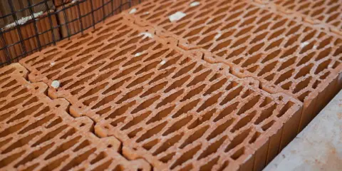 Czerwone pustaki ceramiczne ułożone obok siebie, z siatką zbrojeniową w tle. Zastanawiasz się, ile pustaków na m2 potrzeba do budowy?