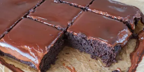 Saftige, vegane Brownies mit glänzendem Schokoladenguss, auf Backpapier zugeschnitten. Ein Traum für jeden Schokoladenliebhaber!