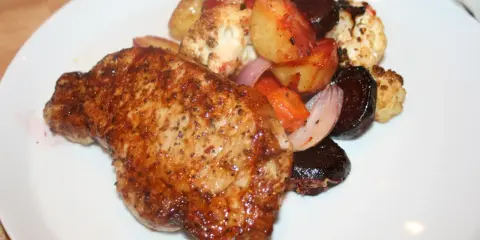 En saftig kotlett i ugn serveras med rostade rotfrukter och blomkål. En härlig middag!