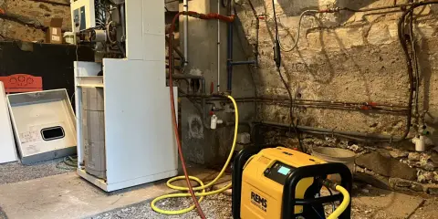 Un technicien effectue le desembouage d'une pompe à chaleur dans une chaufferie. L'équipement est relié à la chaudière par des tuyaux jaunes.