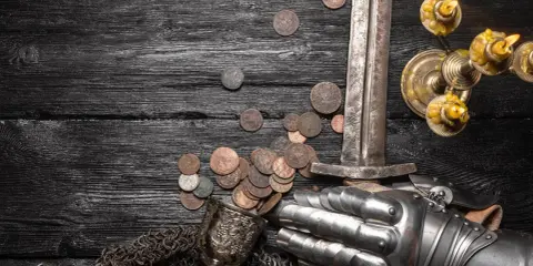 Schwert, Münzen, Ritterhandschuh und Kerzenleuchter auf dunklem Holz. Die Münzen könnten die Vasallen Bedeutung symbolisieren, die für ihren Lehnsherrn kämpften und bezahlten.