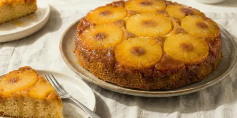 Un gâteau aux ananas facile, doré et caramélisé, avec des tranches d'ananas sur le dessus. Une part est servie sur une assiette avec une fourchette.