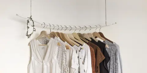 Eine minimalistische **Kapsel Garderobe** mit hellen, gemusterten und erdigen Kleidungsstücken, die an einem Ast hängen.