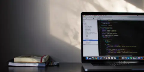 Laptop z kodem w języku C#, gdzie pętla `while` jest kluczowa. Obok leżą notatniki i ołówki.
