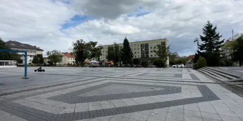 Dziecko na gokarcie przemierza pusty plac, który może być największym rynkiem w Polsce. W tle budynki mieszkalne i drzewa.