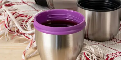Metalowy kubek z fioletową nakrętką i resztkami napoju. Dowiedz się, jak pozbyć się zapachu kawy z termosu, by cieszyć się świeżością.