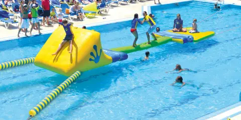 Kinder spielen auf einer aufblasbaren Wasserrutsche und im Pool eines Freibades.