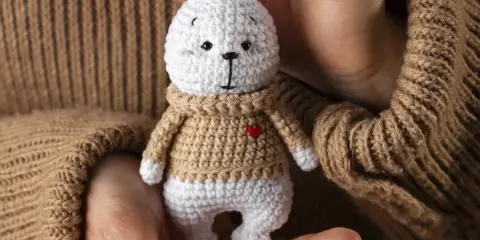 Un tierno conejito blanco con suéter tejido, parte de una colección de amigurumis originales, sostenido entre manos.