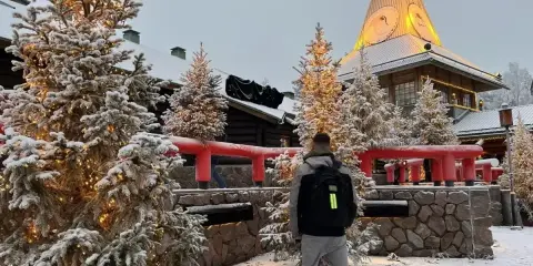 Ośnieżone choinki i budynek z wieżą w Rovaniemi, gdzie mieszka mikołaj. Mężczyzna z plecakiem stoi tyłem.