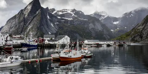 Port de pêche norvégien avec des montagnes imposantes en arrière-plan. Des bateaux de pêche sont amarrés, offrant un mouillage bateau gratuit dans ce paysage pittoresque.