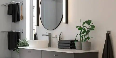 Moderno lavabo con grifería cromada, espejo ovalado y toallas negras. Ideal para una reforma de baño pequeño.