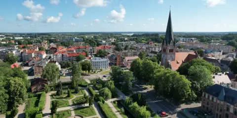 Widok z lotu ptaka na Szczecinek. Widać park miejski z fontanną, kościół z wieżą i zabudowania. To piękne **szczecinek atrakcje** turystyczne.