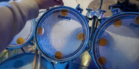 Main d'un batteur ajustant un timbre sur une peau de batterie Evans, prêt à monter une batterie pour un concert.