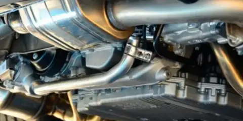 Dettaglio del sistema di scarico di un'auto, con il tubo di scappamento auto lucido e altri componenti metallici.