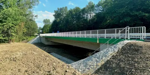 Nowy most na drodze wojewódzkiej 993, z zielonymi elementami i białymi barierkami, otoczony drzewami i skarpami.