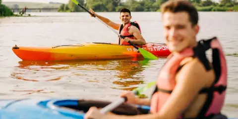 Dwóch uśmiechniętych mężczyzn płynie kajakiem dwuosobowym po jeziorze.