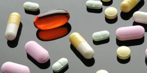Varie pillole e capsule colorate, tra cui una grande capsula arancione trasparente. Un'immagine che fa riflettere sulla terapia biologica cos'è.