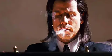 John Travolta i en ikonisk scen från filmer, med rök som virvlar runt hans ansikte.